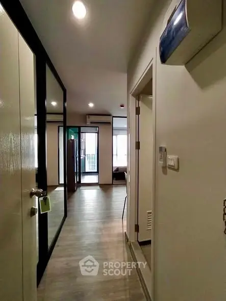 Modern apartment hallway with sleek flooring and mirrored closet doors leading to a bright living area.