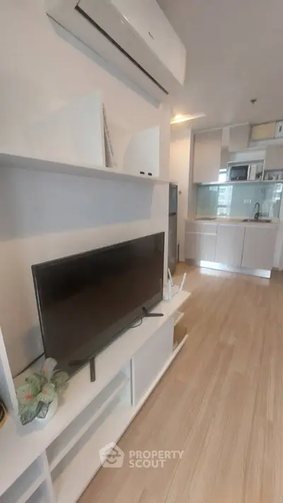 Modern living room with sleek TV unit and open kitchen layout in stylish apartment.