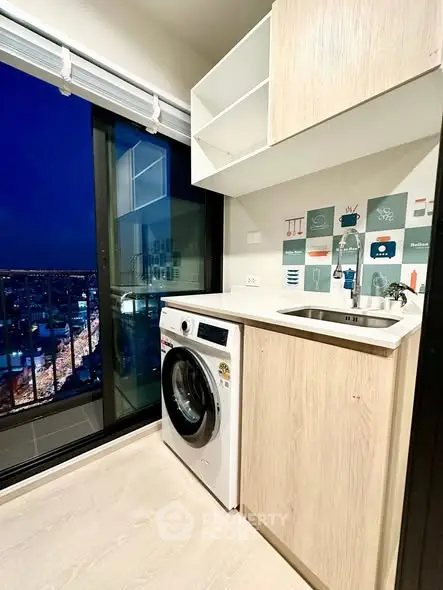 Modern kitchen with washing machine and city view from balcony at night.