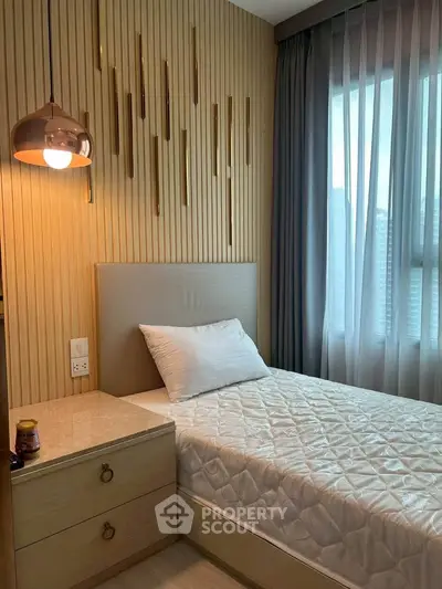 Cozy bedroom with modern decor and natural light, featuring a single bed and stylish lighting.
