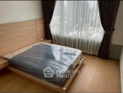 Modern bedroom with large window and city view, featuring a new bed with wooden flooring and elegant curtains.