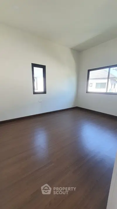 Spacious empty room with wooden flooring and large windows in modern home.