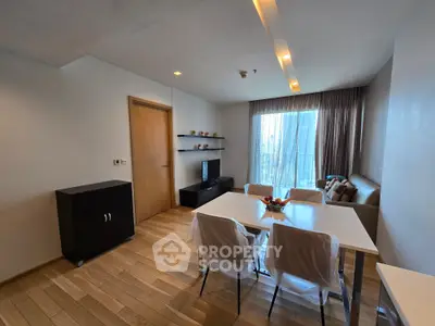 Modern living room with dining area and city view, featuring sleek furniture and wooden flooring.