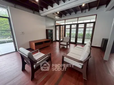Spacious living room with elegant wooden flooring and modern furniture, featuring large windows for natural light.