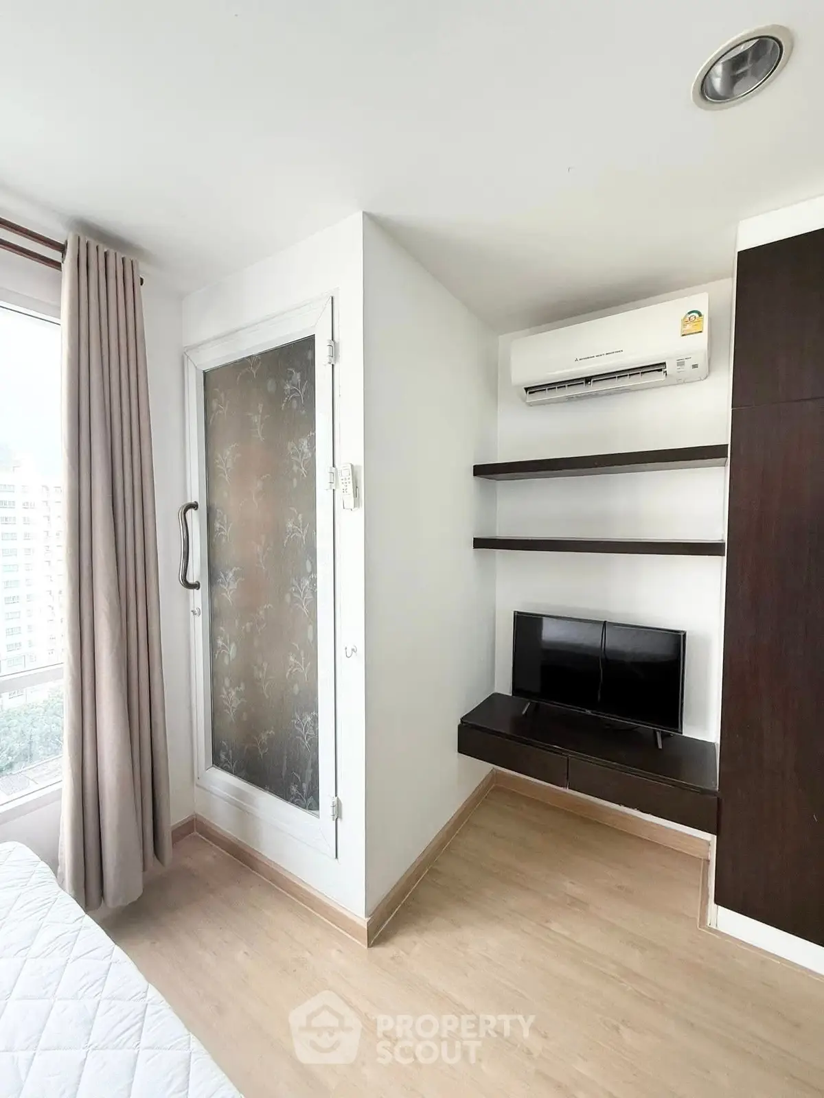 Modern bedroom with air conditioning and built-in TV shelves, featuring a large window with city view.