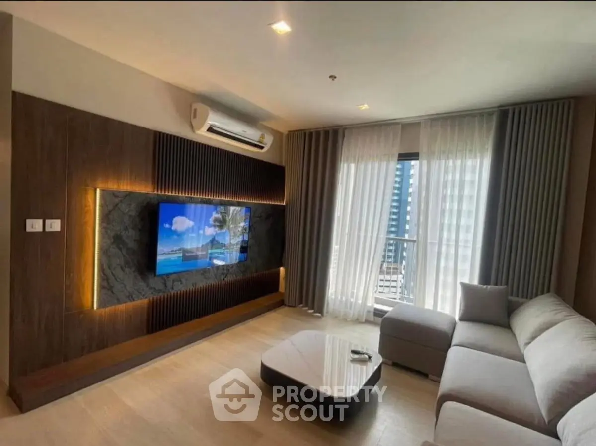 Modern living room with stylish decor, large TV, and natural light from balcony window.