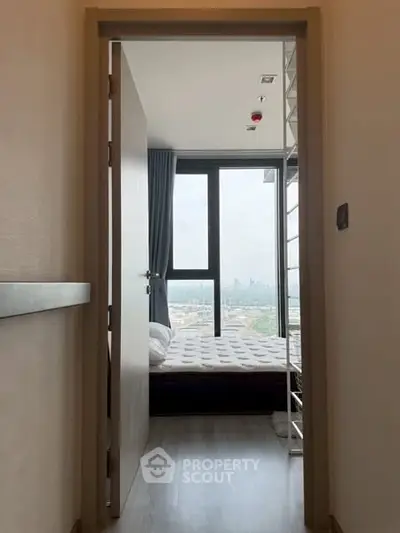 Cozy bedroom with city view through large window, modern design.