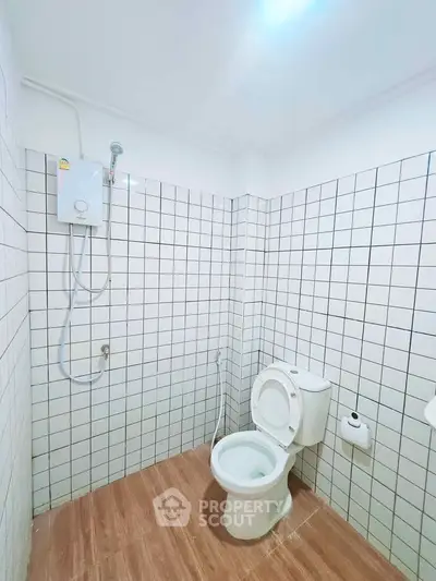 Modern bathroom with white tiled walls and wooden floor, featuring a toilet and shower.