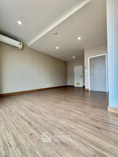 Spacious empty room with wooden flooring and modern air conditioning unit.