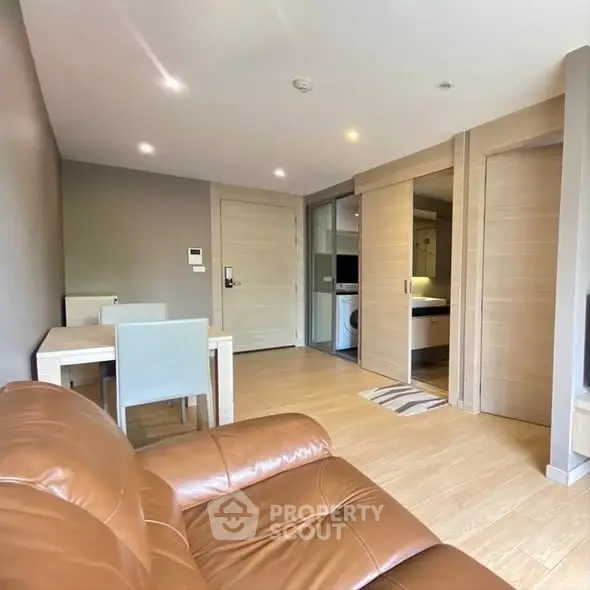 Modern living room with leather sofa and dining area in open layout apartment.