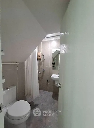 Compact bathroom with shower under staircase, featuring modern fixtures and neutral tiles.