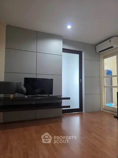 Modern living room with sleek TV setup and wooden flooring, featuring a minimalist design and air conditioning.