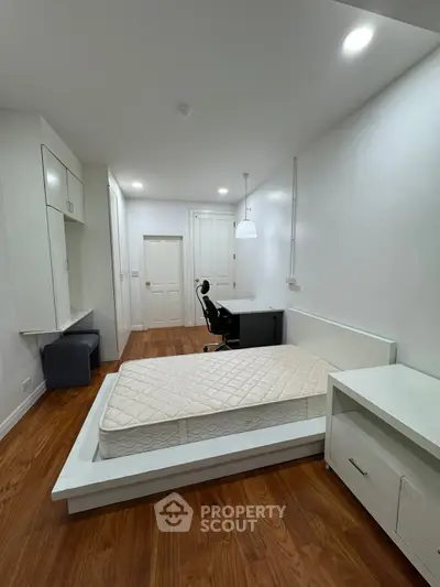 Modern bedroom with wooden flooring, built-in storage, and sleek white furniture.