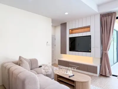 Modern living room with stylish furniture and large TV, featuring a cozy beige sofa and elegant wooden accents.