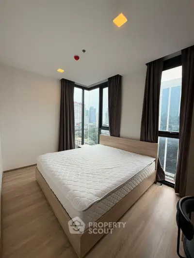 Modern bedroom with large windows and city view, featuring a cozy bed and wooden flooring.
