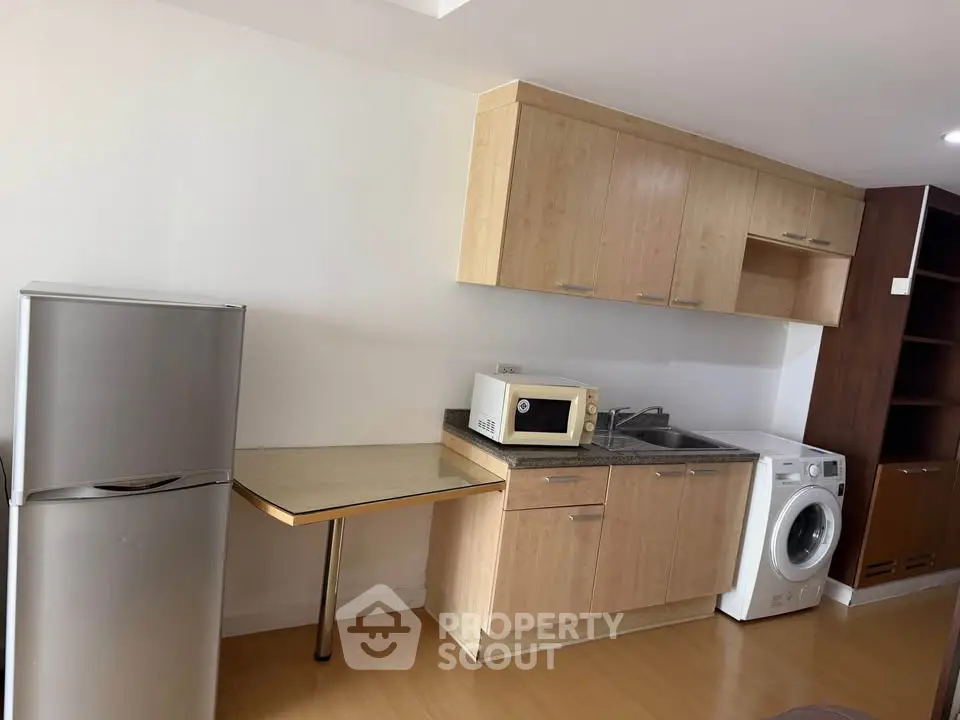 Modern kitchen with wooden cabinets, washing machine, fridge, and microwave in a compact layout.