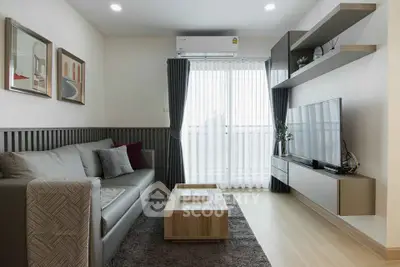 Modern living room with sleek furniture and large TV, featuring stylish decor and natural light from a window.