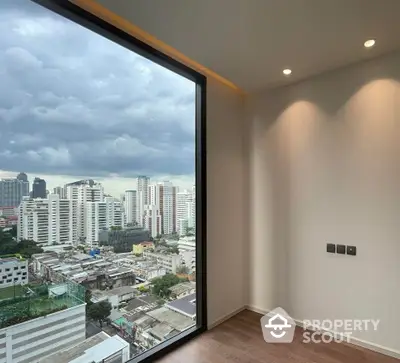 Modern apartment with stunning city view through large window, showcasing urban skyline and wooden flooring.