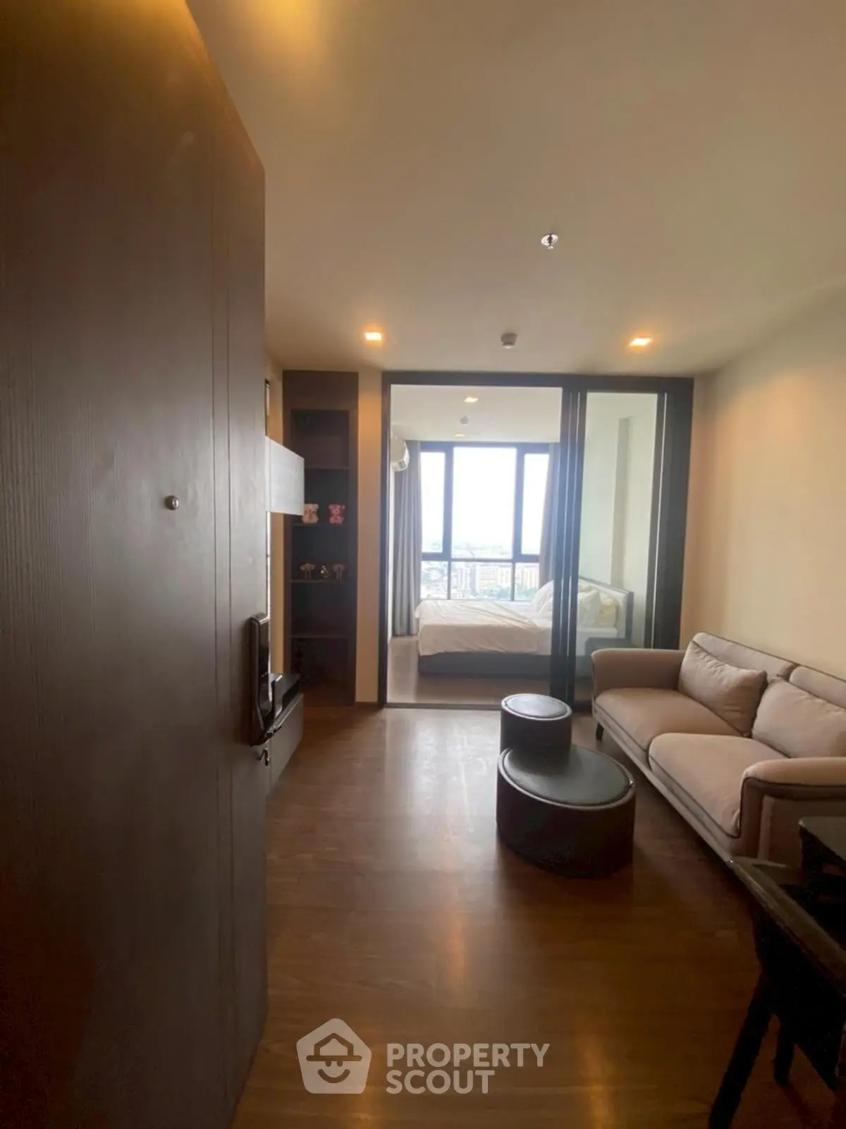 Modern apartment interior with cozy living room and bedroom view, featuring stylish furniture and large windows.