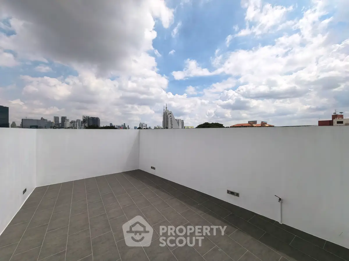 Spacious rooftop terrace with city skyline views under a partly cloudy sky.