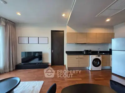 Modern living room with open kitchen, featuring sleek appliances and wooden flooring.