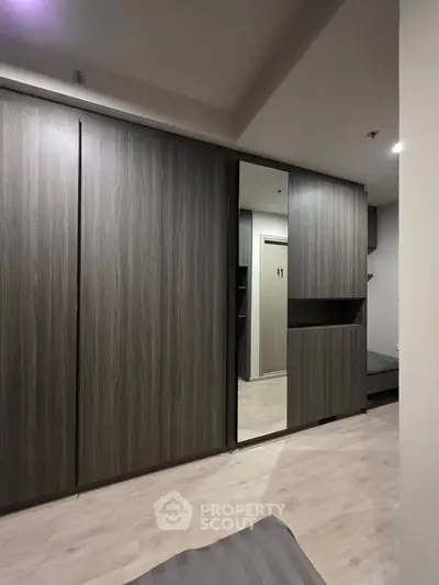 Modern bedroom with sleek wooden wardrobe and mirror, showcasing minimalist design and ample storage space.