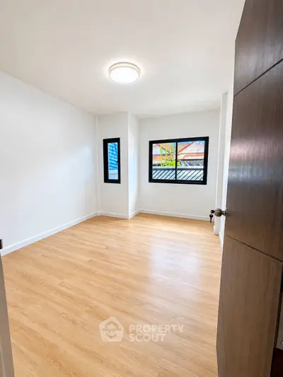 Spacious empty bedroom with wooden flooring and large windows for natural light.