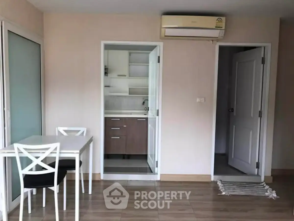Modern apartment interior with dining area and kitchen, featuring sleek furniture and air conditioning.