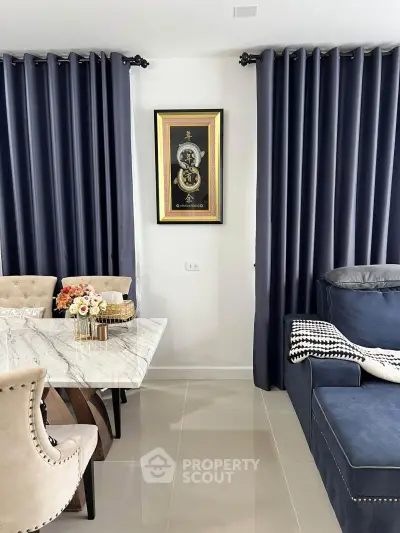 Elegant dining and living area with marble table and plush seating, featuring stylish decor and dark curtains.