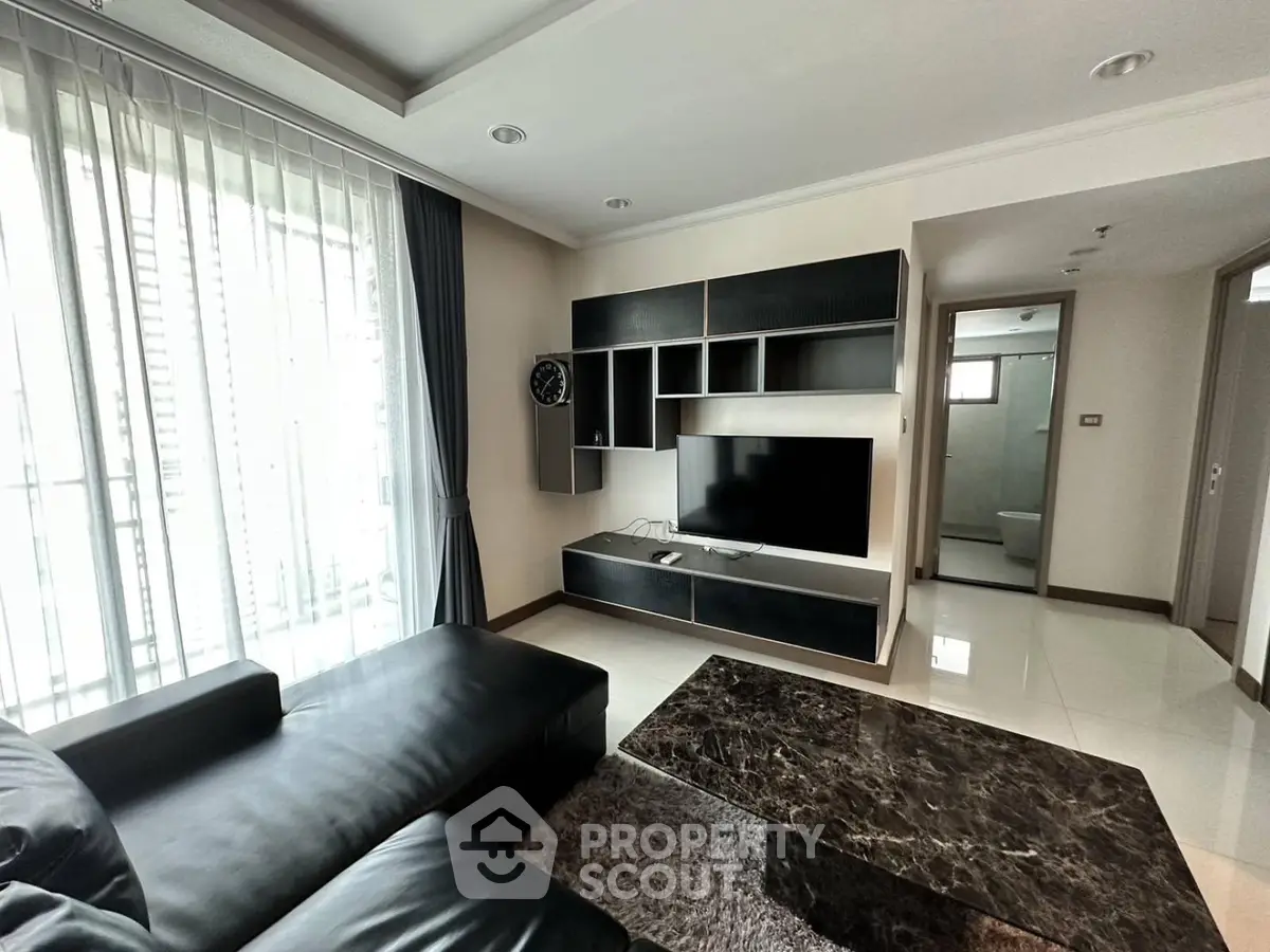 Modern living room with sleek black furniture and large TV, featuring elegant marble coffee table and natural light.