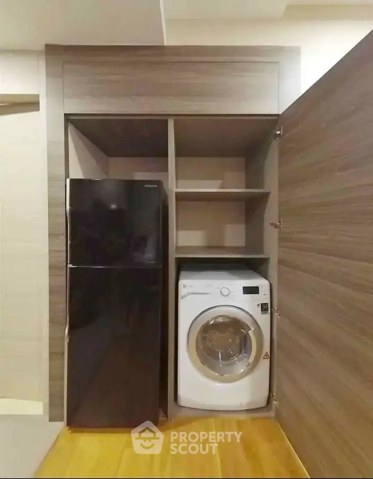 Compact laundry and storage area with modern washing machine and fridge in sleek cabinetry.
