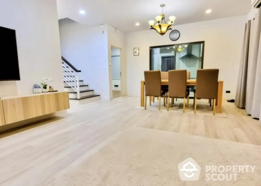 Spacious living room with modern dining set, elegant lighting, and staircase leading to upper level, perfect for family gatherings.