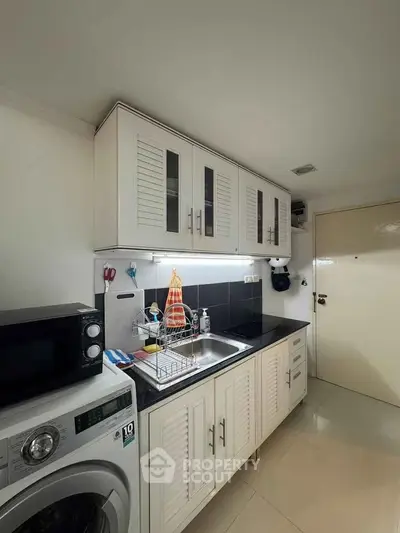 Modern kitchen with sleek cabinets and appliances, featuring a washing machine and microwave.