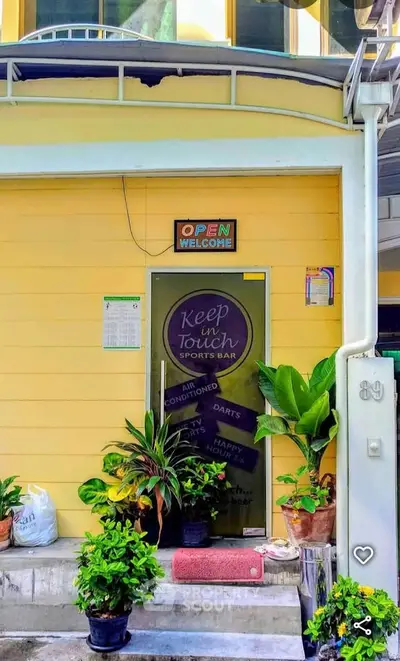 Charming yellow exterior of a sports bar with lush plants and welcoming entrance.