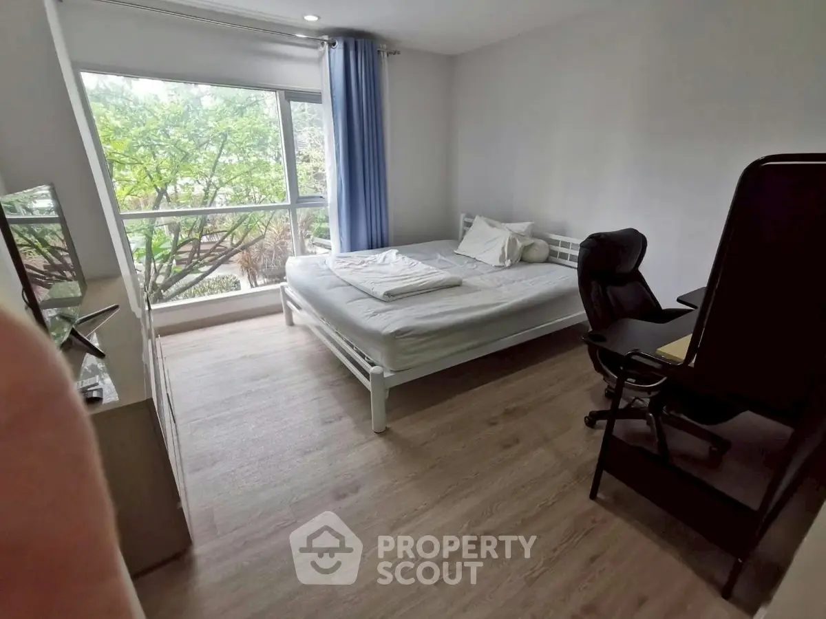 Spacious bedroom with large window and modern furnishings, offering a serene view of lush greenery.