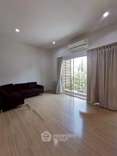 Spacious living room with wooden flooring and balcony access in modern apartment.