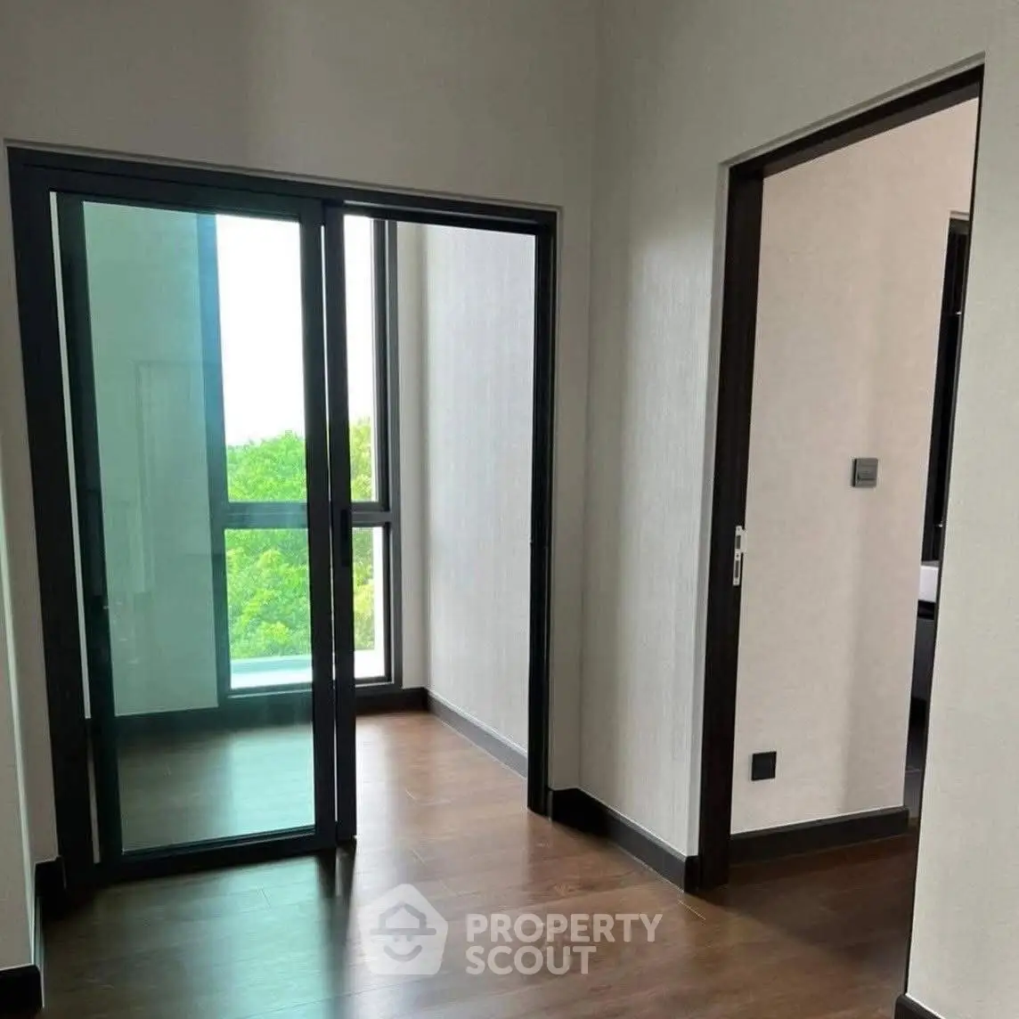 Modern apartment interior with glass doors leading to a balcony, featuring sleek wooden flooring.