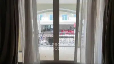 Elegant balcony view through large window with sheer curtains in modern apartment.