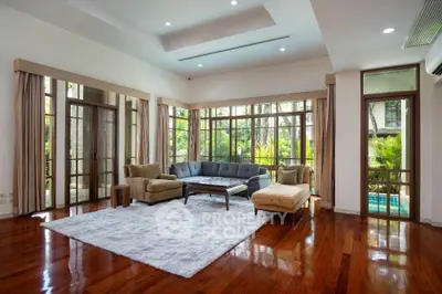 Spacious living room with hardwood floors and large windows overlooking lush greenery.