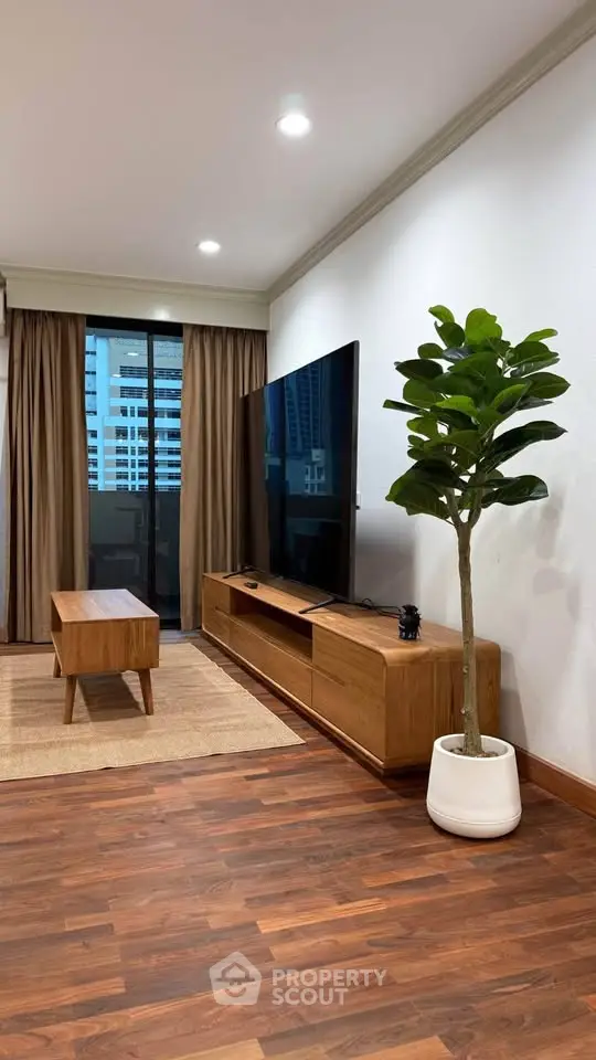 Modern living room with sleek wooden furniture and large TV, featuring a stylish indoor plant and city view.