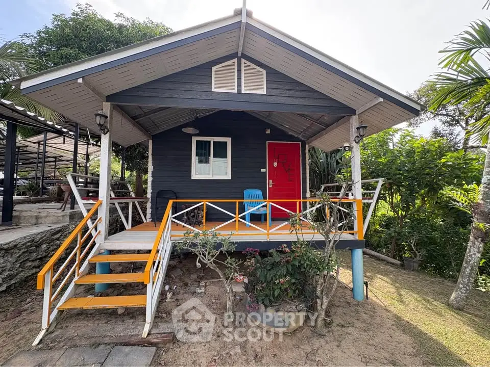 Charming small house with vibrant red door and cozy porch in lush garden setting.