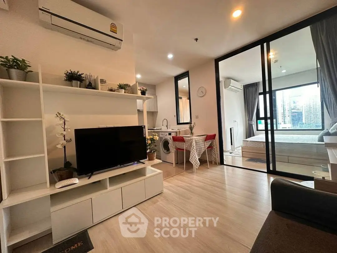 Modern open-plan living room with TV, dining area, and bedroom view.