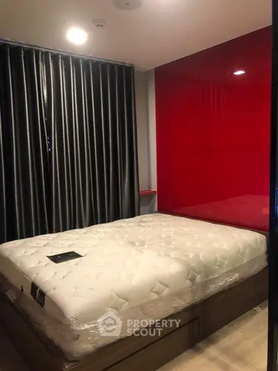 Modern bedroom with red accent wall and plush mattress in stylish apartment.