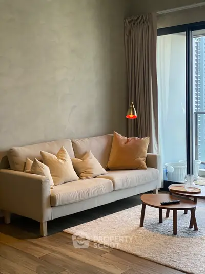 Cozy living room with beige sofa, stylish cushions, and a small wooden coffee table near a balcony.