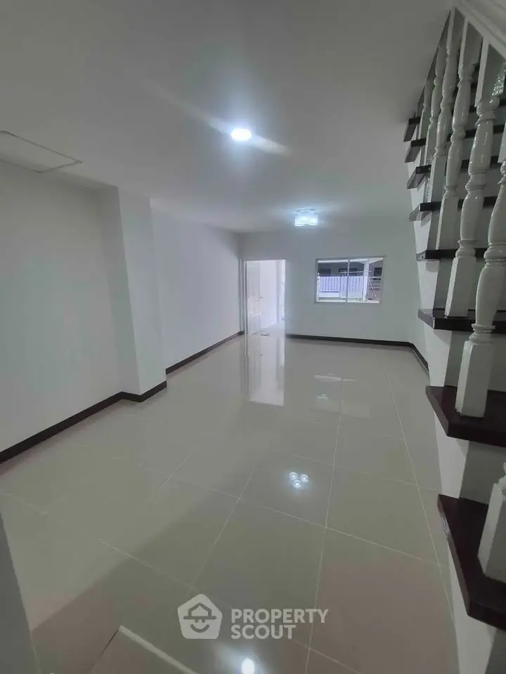 Spacious modern living room with sleek tiled flooring and elegant staircase, perfect for family gatherings.