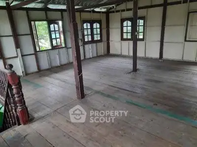 Spacious rustic interior with wooden flooring and large windows, ideal for renovation.