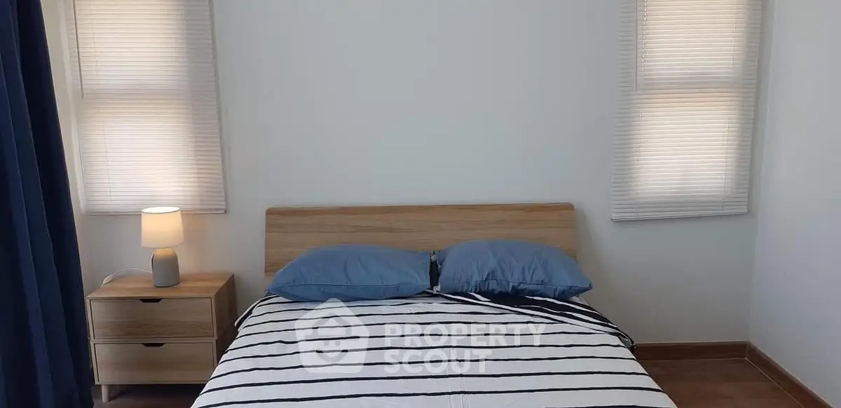 Cozy bedroom with modern wooden bed and nightstand, featuring striped bedding and soft lighting.