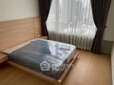 Modern bedroom with large window and city view, featuring a new bed with plastic cover.