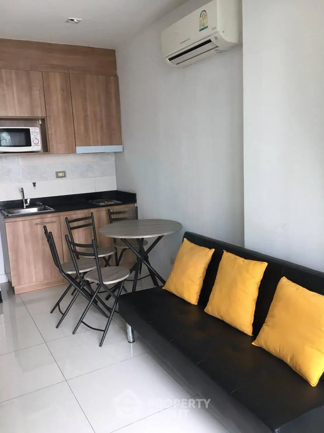 Modern compact kitchen and living area with sleek black sofa and yellow cushions.