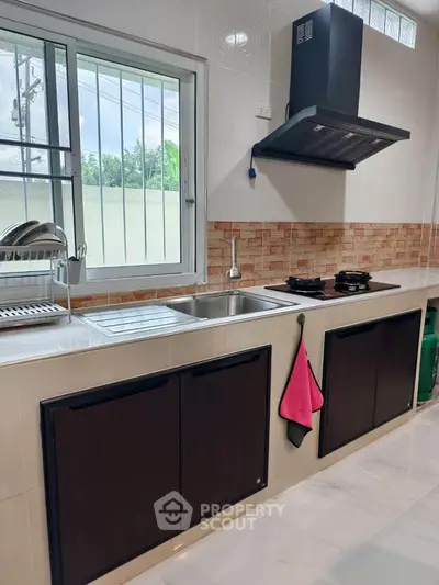 Modern kitchen with sleek cabinetry and gas stove, featuring a large window for natural light.